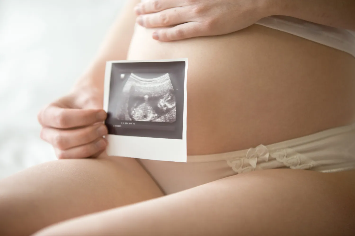 Mujer embarazada sosteniendo una ecografía en su abdomen, simbolizando la alegría de la maternidad y el desarrollo fetal.